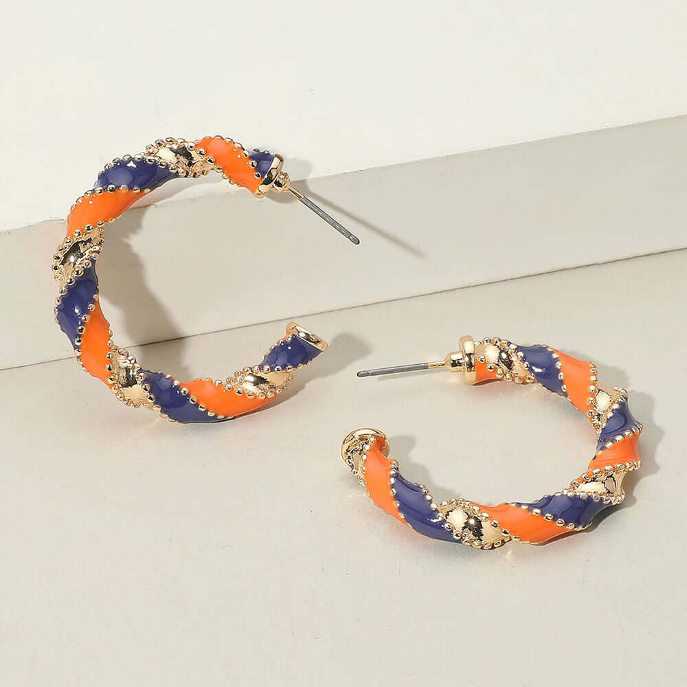 The Playmaker Charm - Orange & Purple Earrings feature alternating orange and purple enamel with gold bead accents on a light beige surface—hypoallergenic hoops perfect for game day style.