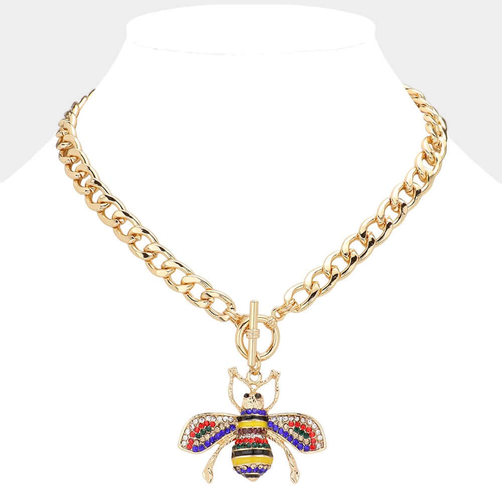 The Queen Bee Luxe - Gold & Multi Necklace features a chunky chain with a toggle clasp and a vibrant gemstone bee pendant, adding playful rainbow flair, beautifully showcased on a white mannequin bust.