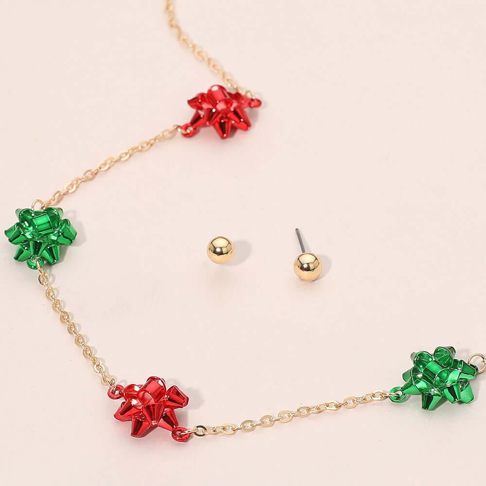 The All Smiles - Gold Multi Necklace, featuring red and green metallic bows, is paired with gold ball stud earrings for a festive holiday jewelry look on a light background.