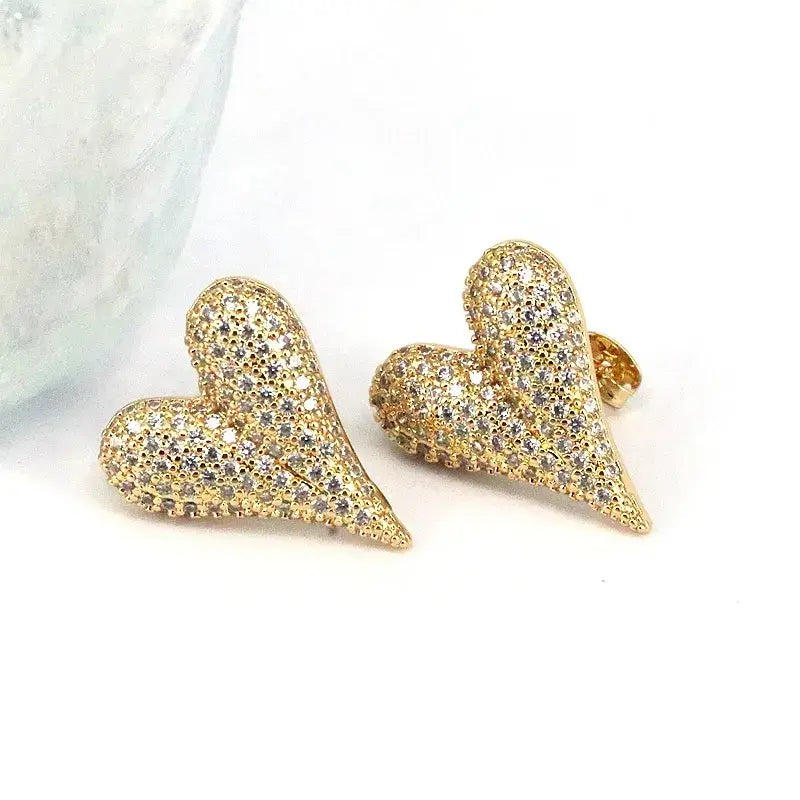 The Love Spark - Gold Heart Post Earrings, featuring small sparkling crystals, are a romantic accessory displayed elegantly on a white surface.