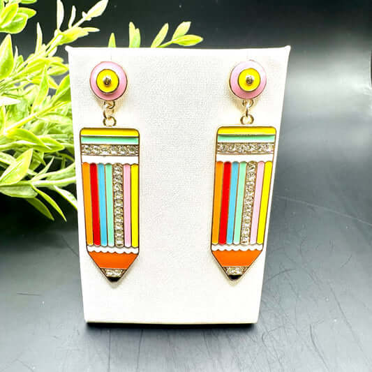 Bright Idea - Multi Earrings: Vibrant pencil earrings with vertical stripes in orange, yellow, green, blue, red, and silver—displayed on a white stand with green leaves. Perfect teacher gift for back-to-school!.