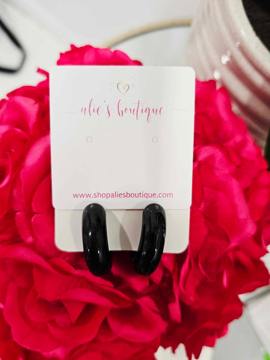A pair of Chaotic Chic - Black Marble Acrylic Resin Hoop Earrings - WW is displayed on a white card with "alies boutique" in pink, set against vibrant pink flowers. Find these trendy earrings at shopaliesboutique.com.