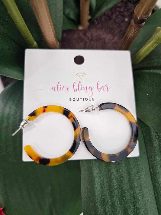 Chaotic Chic - Brown & Black Acrylic Resin Hoop Earrings are shown on a white alics bling bar BOUTIQUE card, with green leaves in the background.