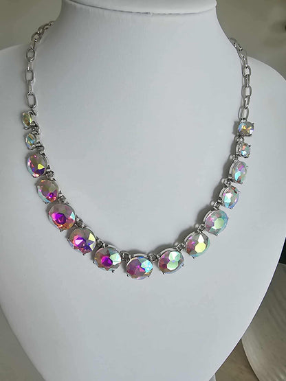 The Aurora Pop - Iridescent Necklace features bold, round iridescent gems in pink, green, and yellow on a silver chain, elegantly presented on a white bust stand.