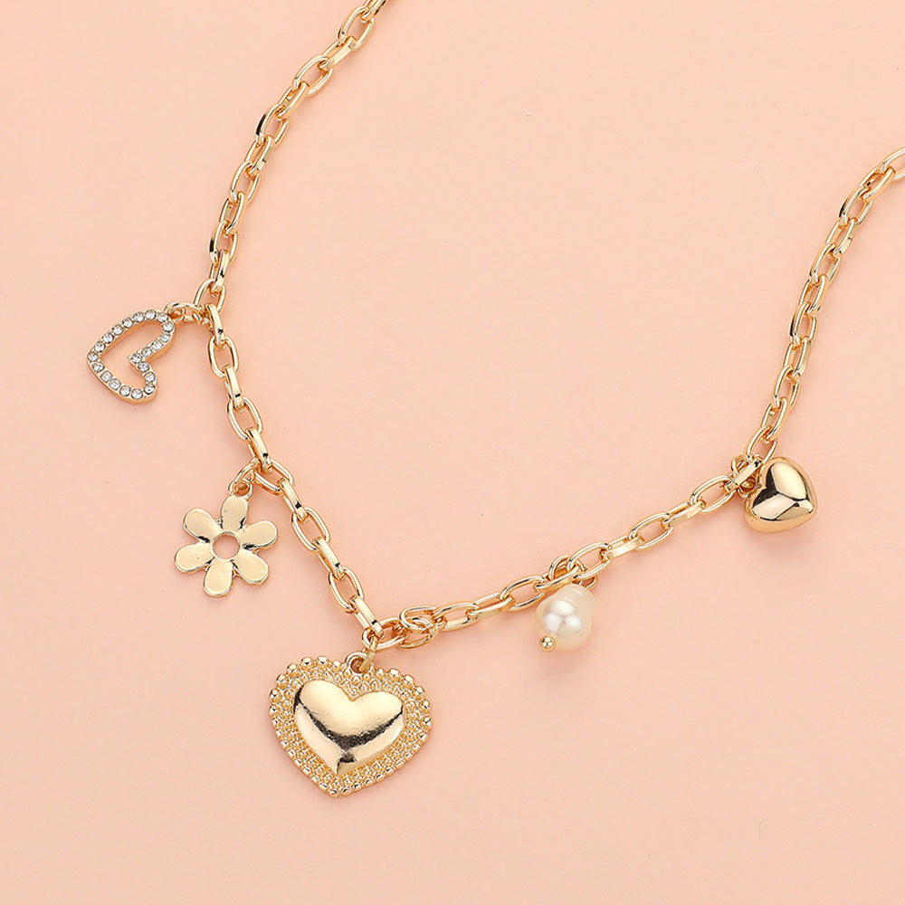 The Love Blossoms - Gold Charm Necklace features five elegant charms—a rhinestone heart, gold flower, large gold heart, pearl bead, and solid gold heart—displayed on a soft pink background.