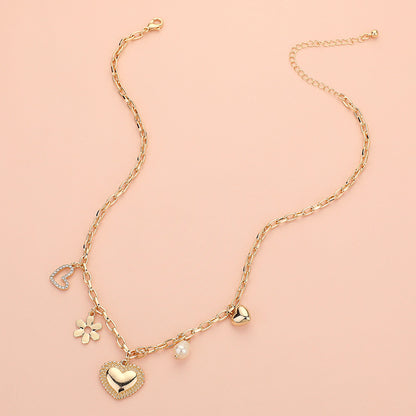 Introducing Love Blossoms - Gold Charm Necklace: a stunning piece with a crystal-studded heart, daisy flower, pearl bead, and golden heart, all showcased on a soft pale pink background for an elegant touch.