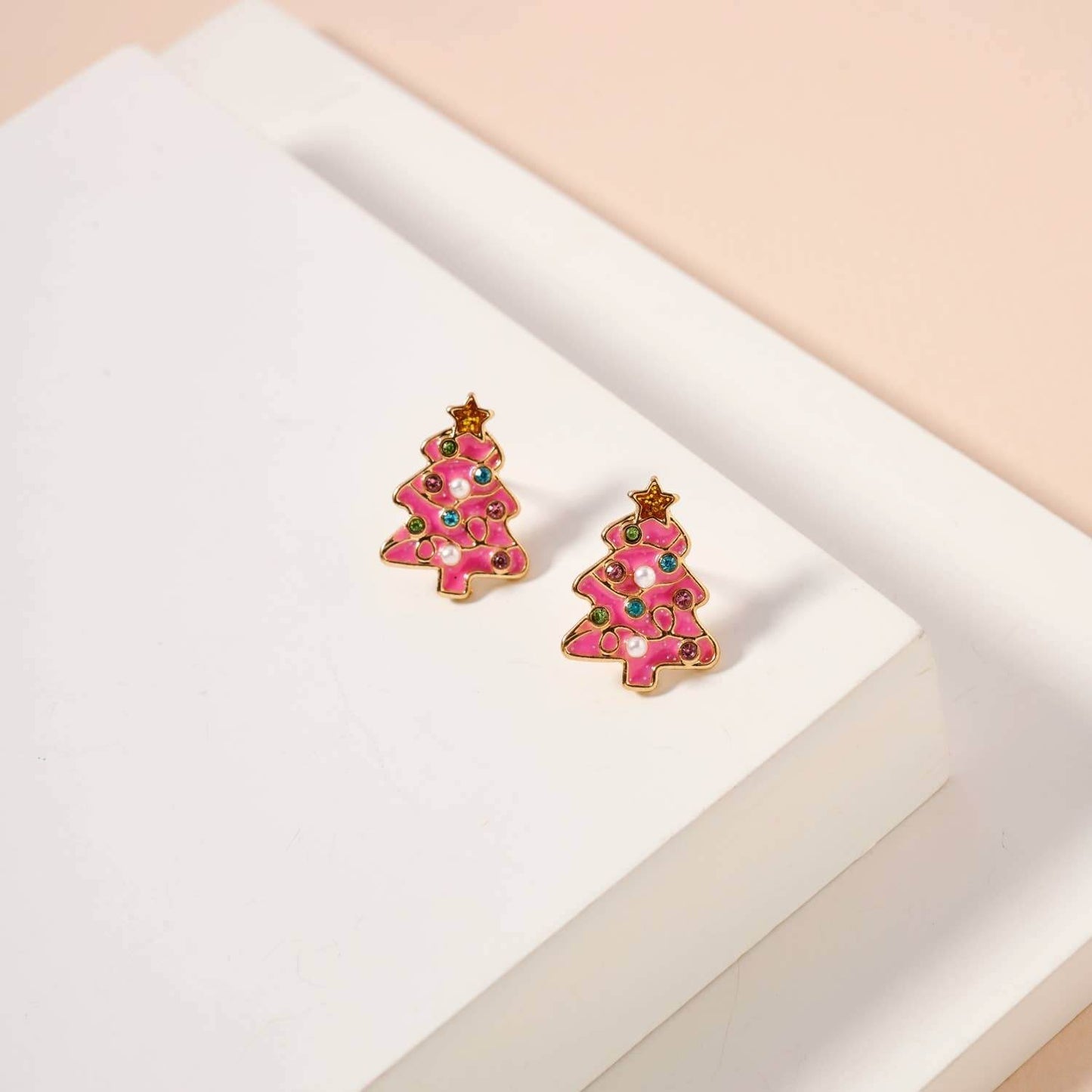Pink Christmas tree earrings on a white and beige background