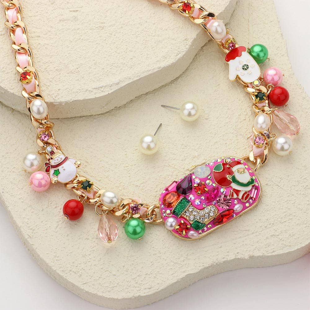 The Jingle Luxe - Holiday Glam Necklace features colorful beads, pearl accents, Christmas charms, and a bold Santa pendant. Matching pearl stud earrings complete the festive look on a cream-textured surface.