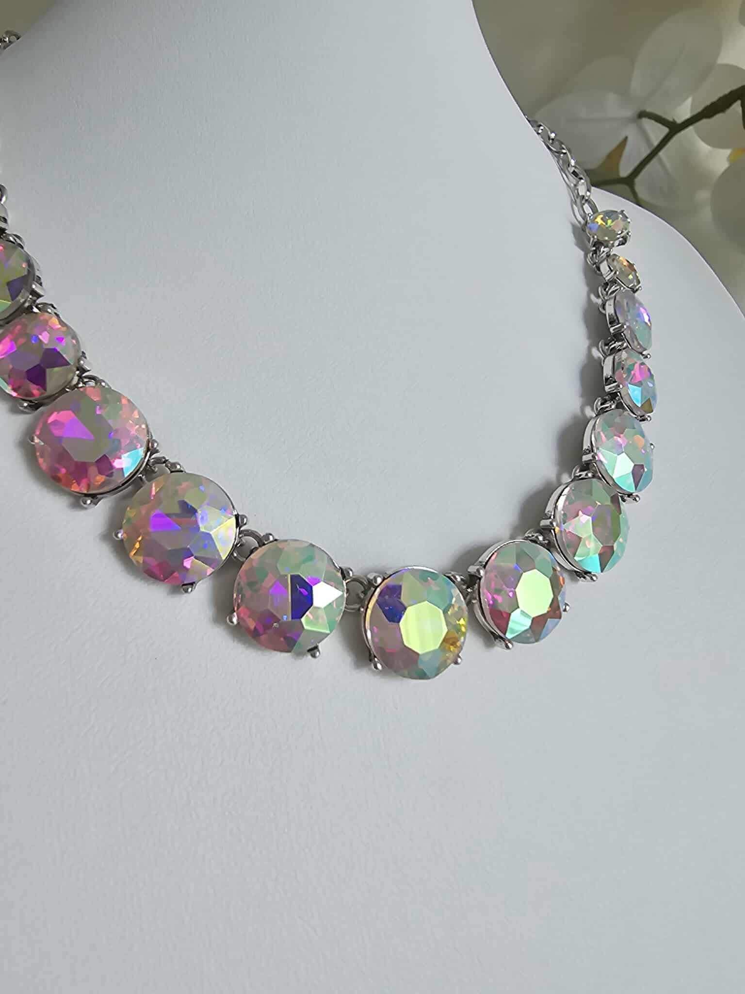 A close-up of the Aurora Pop - Iridescent Necklace, a statement piece with large faceted iridescent gems in silver settings, shown on a white mannequin bust.