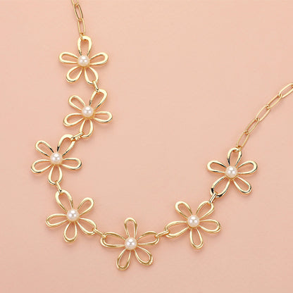 The Pure Bloom - Gold Flower Necklace features five open-petal charms accented with white pearls on an elongated oval-link chain, beautifully displayed against a light peach background.