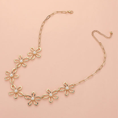 The Pure Bloom - Gold Flower Necklace features five daisy-shaped charms with white pearl centers on a chain-link design, adjustable for the perfect fit. Displayed on a light peach background, this elegant piece adds a graceful touch to any look.