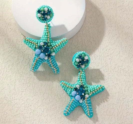 Shoreline Shimmer - Blue Seed Bead Starfish Earrings: two intricately beaded turquoise, blue, and white earrings displayed on a textured background. Perfect ocean-inspired statement jewelry—now on Labor Day Sale!.